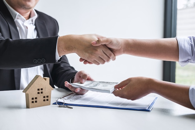 Photo image of successful deal of real estate, broker and client shaking hands after signing contract approved application form, concerning mortgage loan offer for and house insurance.