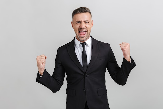 Image of successful delighted businessman in formal suit screaming and clenching his fists isolated