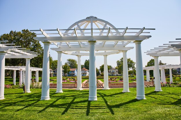 image of sunny summer day with white pergola in lakeside park with flowers behind it