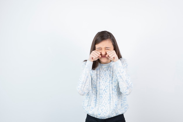 Image of teen girl in sweater standing and crying over white.