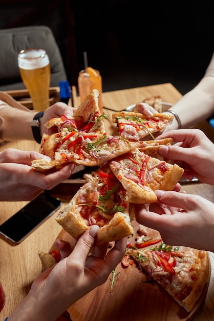 Image of teenage friends hands taking slices of pizza