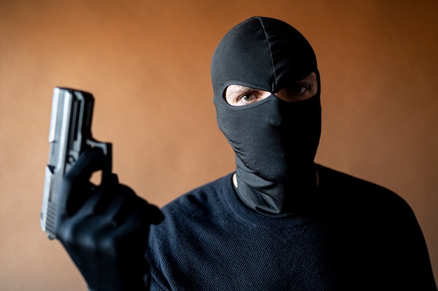 Foto immagine di un ladro con passamontagna e pistola in mano