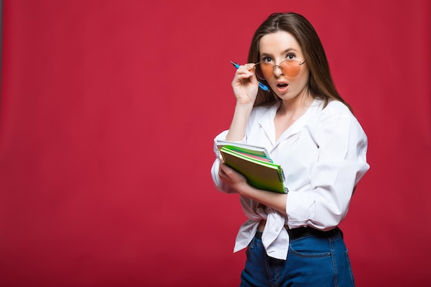 Image of thinking dreaming thoughtful young woman isolated over red wall background writing notes