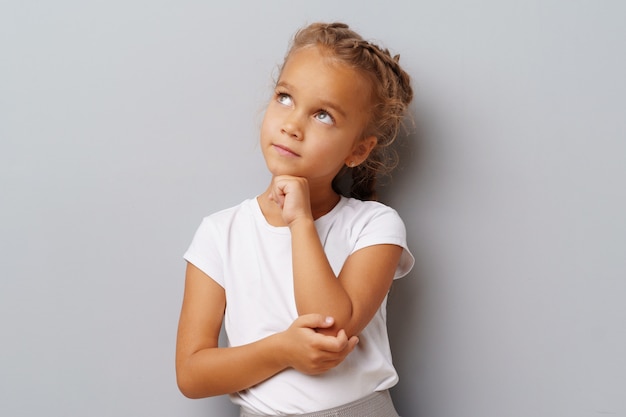 Photo image of thinking little girl standing over a gray background