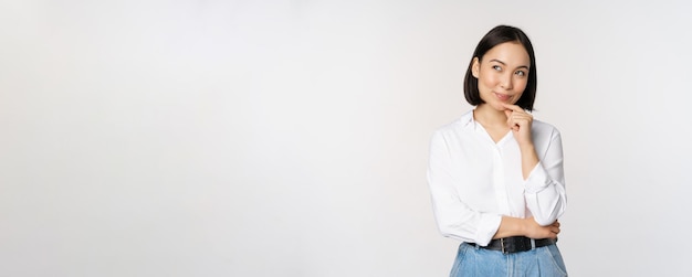 Image of thoughtful smiling woman has an idea scheming planning looking aside and thinking standing in office white blouse against studio background