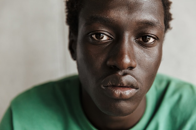 Image of thoughtful young african american man in casual clothes sitting over wall at home