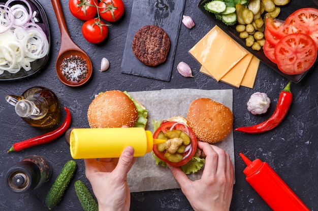 Image on top of two hamburgers and human hands adds the mustard into the burger