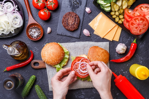 Image on top of two hamburgers, human hands and ingredients