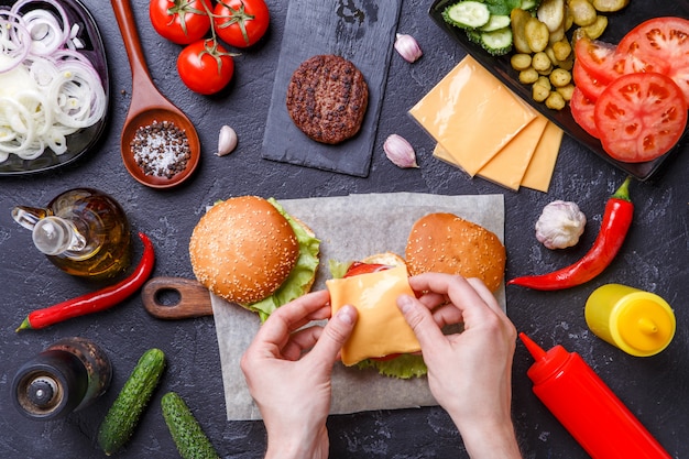 Image on top of two hamburgers, human hands and ingredients