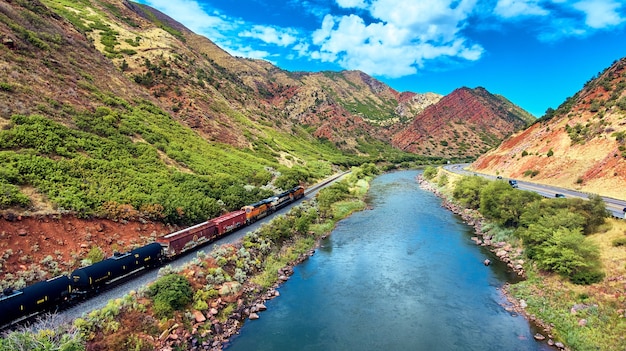 Image of Train driving through valley of red mountains with river