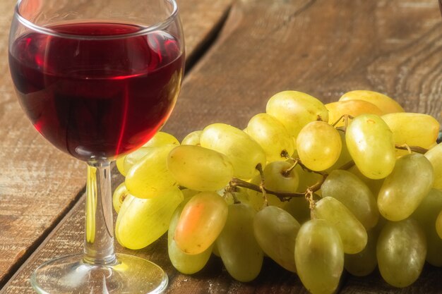 An image of two drinking glasses with red wine  and a bunch of grape