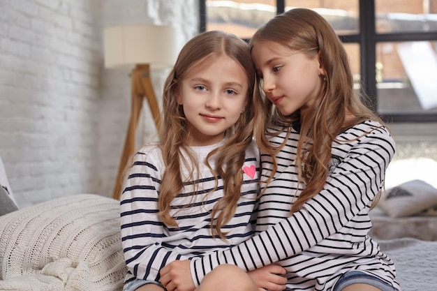 The image of two little sisters sitting on the bed in the room