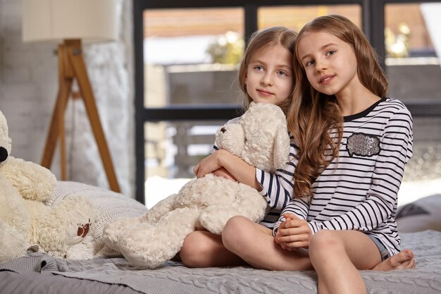 The image of two little sisters sitting on the bed in the room