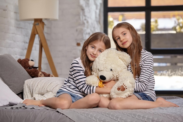 The image of two little sisters sitting on the bed in the room