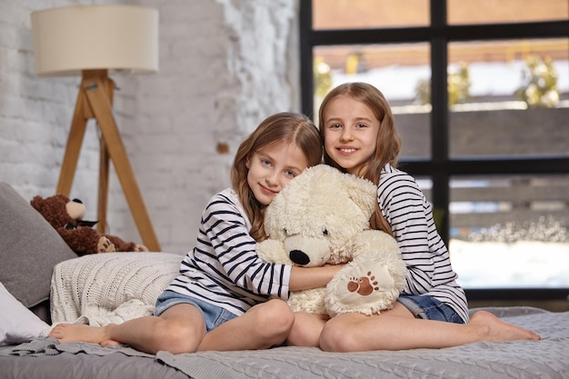 The image of two little sisters sitting on the bed in the room