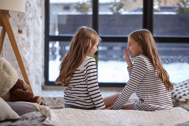 The image of two little sisters sitting on the bed in the room