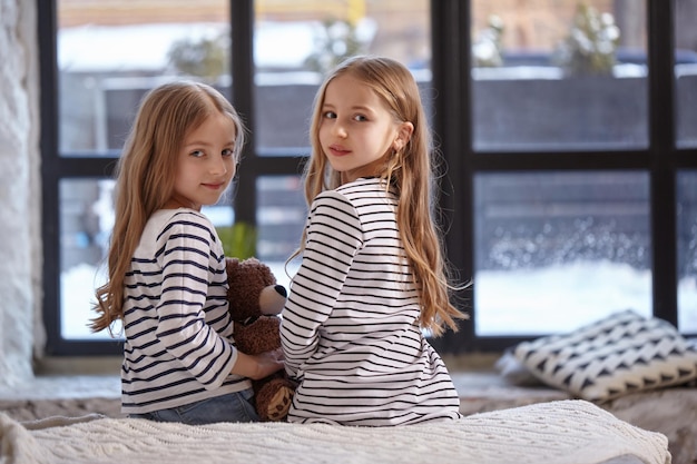 The image of two little sisters sitting on the bed in the room