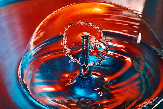 Foto immagine di due gocce d'acqua che si incontrano nell'aria all'interno della bolla su acqua blu e rossa