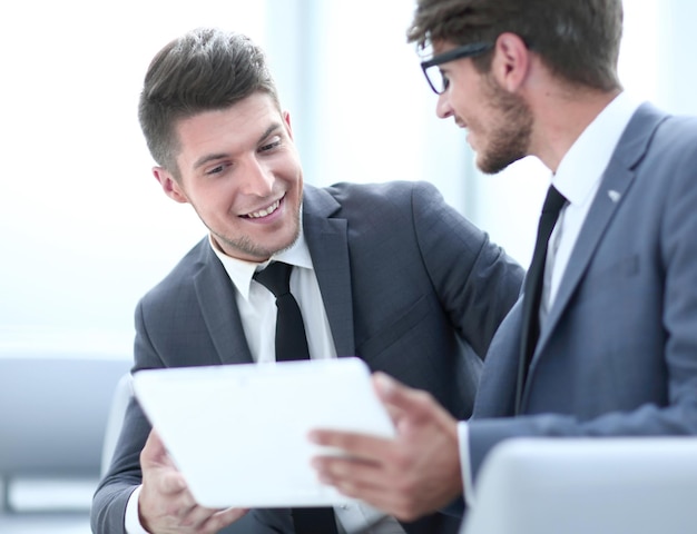 Image of two young businessmen using touchpad at meeting