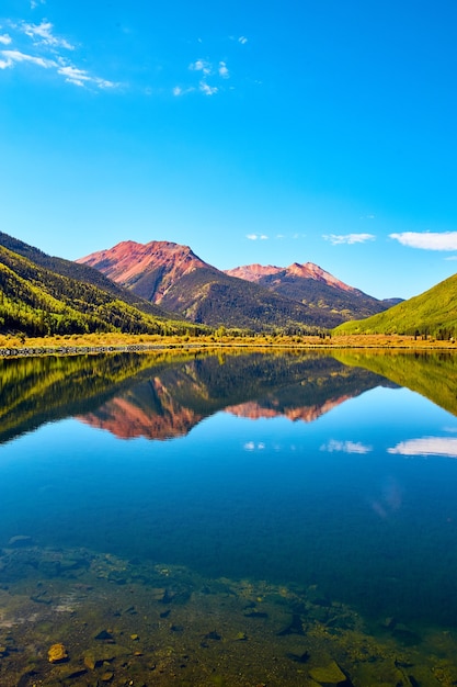 Image of vertical landscape of lake in the mountains with fall aspen trees and red sandy mountain peaks against blue sky