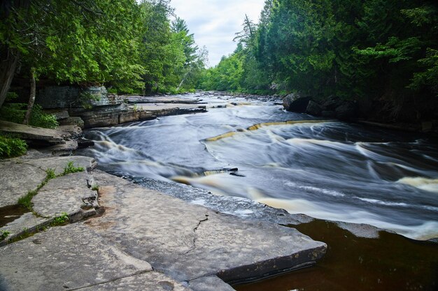 灰色の岩に沿って小さな滝が流れ落ちる川の眺めの画像