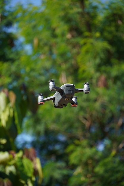 Image of white and gray drone flying, with trees and sky around.