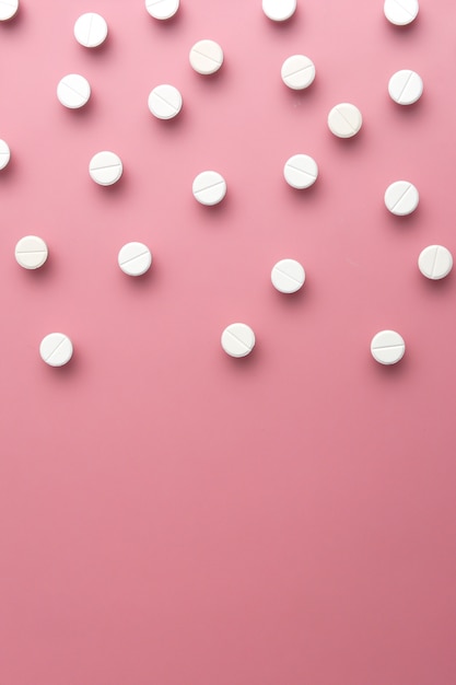 Photo image of white pills on pink background. copy space. flat lay. vertical composition.