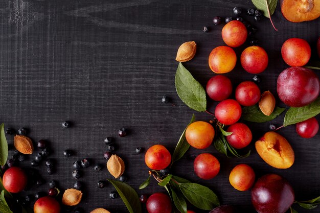 Image with beautiful composition of blueberries, plums, aliches and green leaves on dark concrete surface. Delicious friut on dark surface. Top view. Halthy eating concept. Copy space for promotion