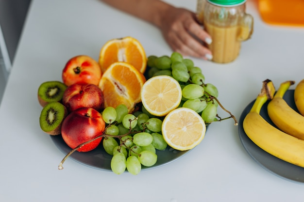 Изображение с фруктовыми ингредиентами, лежащими в таблице. Женская рука с бокалом смузи