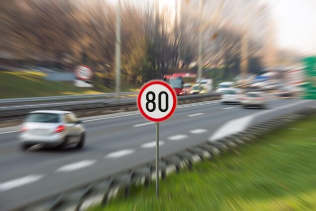 Foto immagine con effetto zoom che mostra un segnale stradale con limite di velocità di 80 km/h su un'autostrada piena di auto