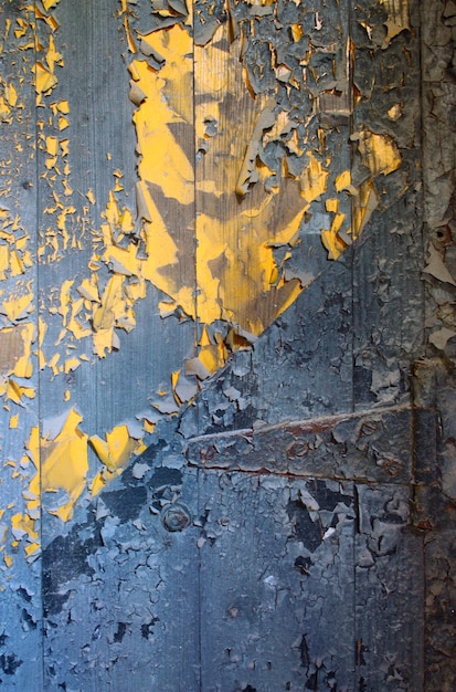 Image of Wooden door's blue paint peels to show bright yellow paint beneath
