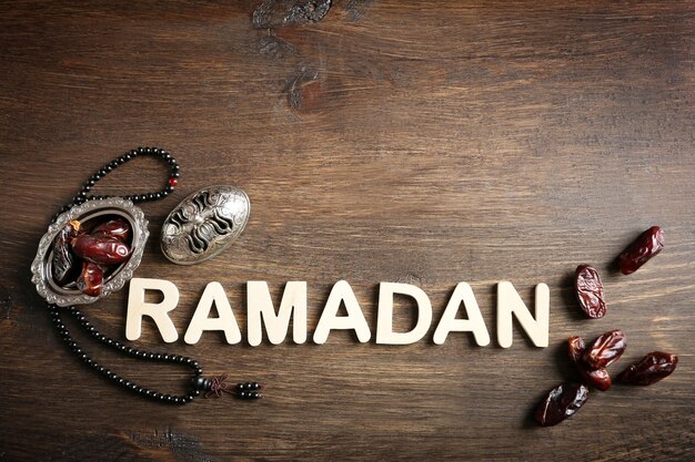 Foto immagine della parola ramadan con rosario e frutta di datteri su sfondo di legno da vicino