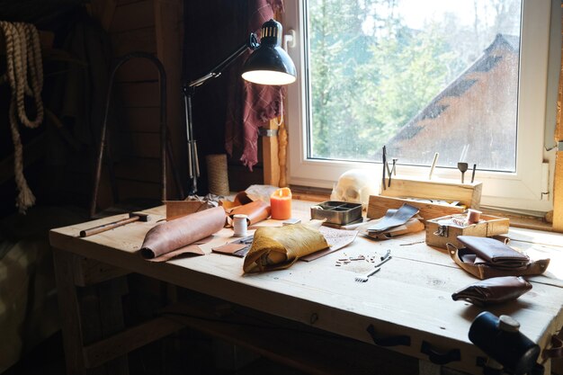 Image of workplace of carpenter with work tools and pieces of leather material on the table in workshop