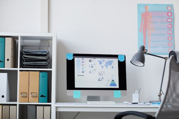 Image of workplace with computer monitor on it and medical posters on the wall at office