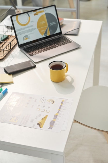 Image of workplace with laptop documents and cup of coffee at office