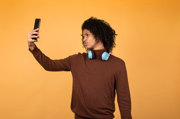 電話でselfieを取っている黄色の背景の上に孤立してポーズをとっている若いアフリカ系アメリカ人の男性の画像。