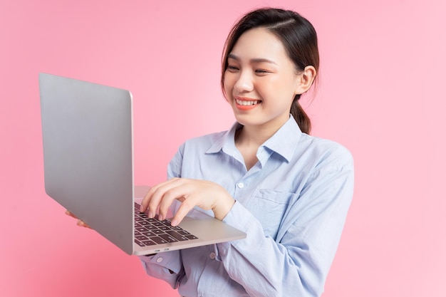 Image of young Asian business woman holding laptop on pink background