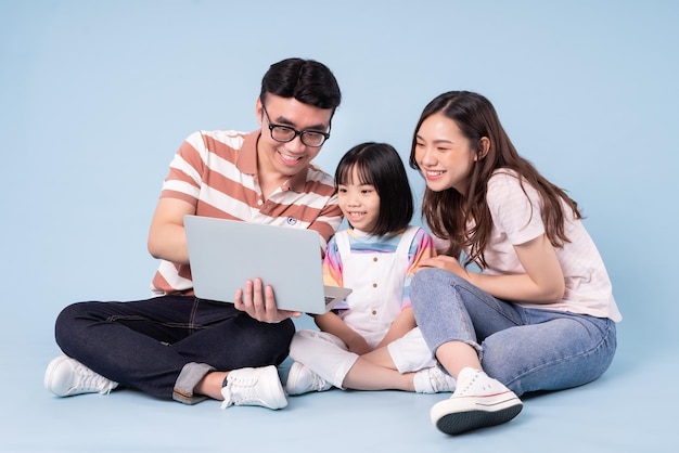 青い背景の上のラップトップを使用して若いアジアの家族の画像
