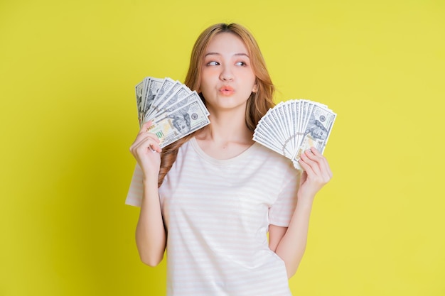 Изображение молодой азиатской девушки с деньгами на желтом фоне