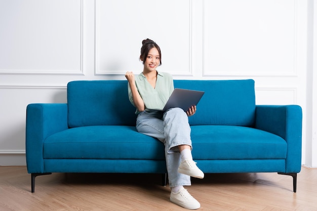 изображение молодой азиатской девушки, сидящей дома на диване