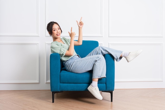 изображение молодой азиатской девушки, сидящей дома на диване