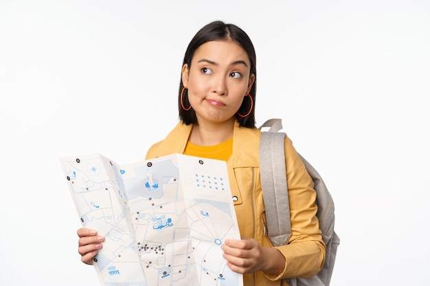 Image of young asian girl tourist traveller with map and backpack posing against white studio background