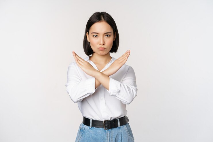Photo 흰색 배경 위에 서 있는 것을 거부하는 정지 십자가 금지 표지판을 보여주는 젊은 아시아 한국 여학생의 이미지