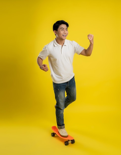 Image of young asian male playing skateboard on a yellow background