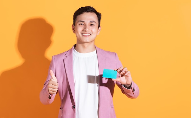 Image of young Asian man holding bank card atm card on background