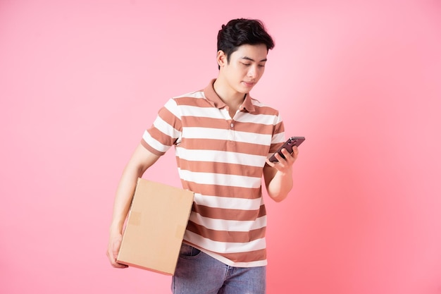 Image of young Asian man holding cardboard on pink background