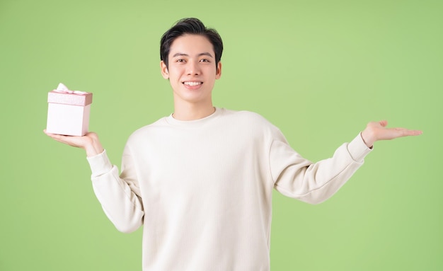 Image of young Asian man holding giftbox on background