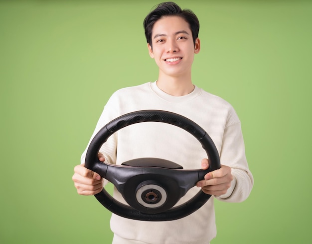 Image of young Asian man holding steering wheel on background