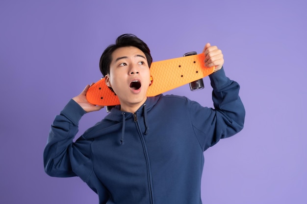 보라색 배경에서 스케이트보드를 타는 젊은 아시아 남자의 이미지