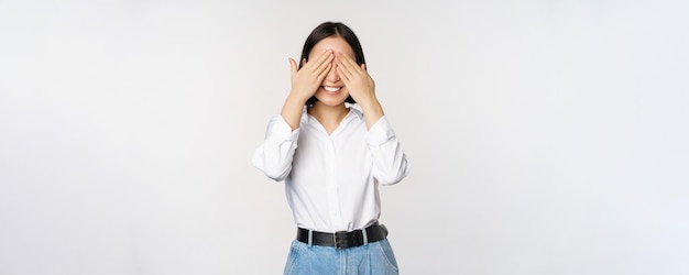 Image of young asian woman close her eyes and smiles waits for surprise anticipates stands over white background